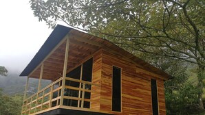 Een houten hut met een balkon, gebouwd op palen in een bebost gebied met uitzicht op het omliggende landschap.