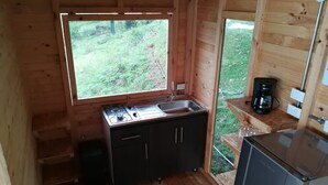 Een knus houten vakantiehuisje met een kitchenette, inclusief een spoelbak, fornuis en keukenkastjes.