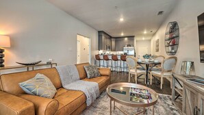 A modern living room with a brown leather sofa, a glass coffee table, and a dining area with a white table and chairs. - Single-Story Condo < 1 Mile From Downtown! (Fredericksburg)
