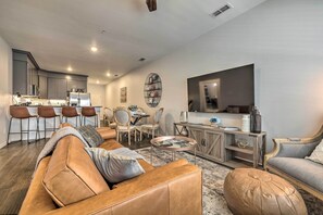 A modern living room with a leather sofa, a coffee table, and a dining area with chairs and a kitchen in the background.