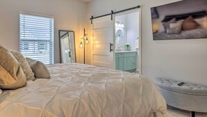 A bedroom with a bed, a sliding door to a bathroom, a mirror, and a television on the wall. - Single-Story Condo < 1 Mile From Downtown! (Fredericksburg)