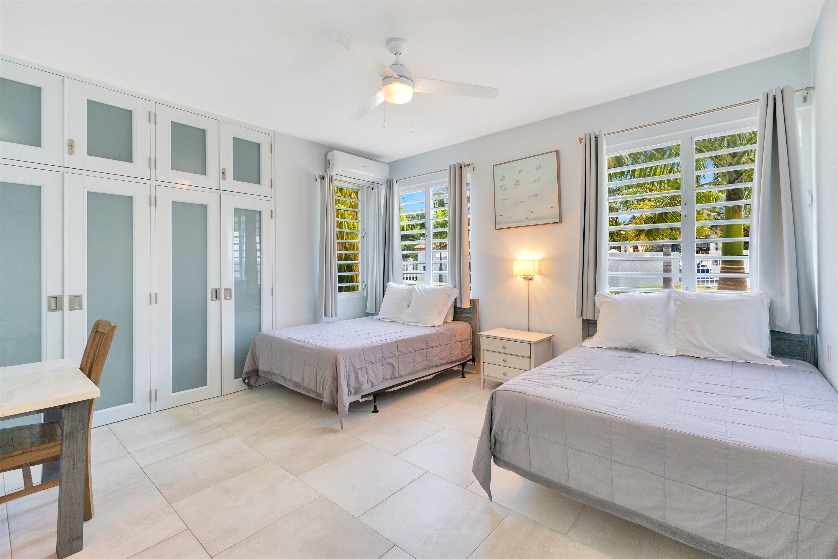 A bedroom with two beds, a ceiling fan, and a window with curtains.
