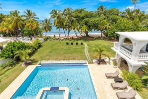 A pool area with lounge chairs, a small pool, and a view of the beach and palm trees.