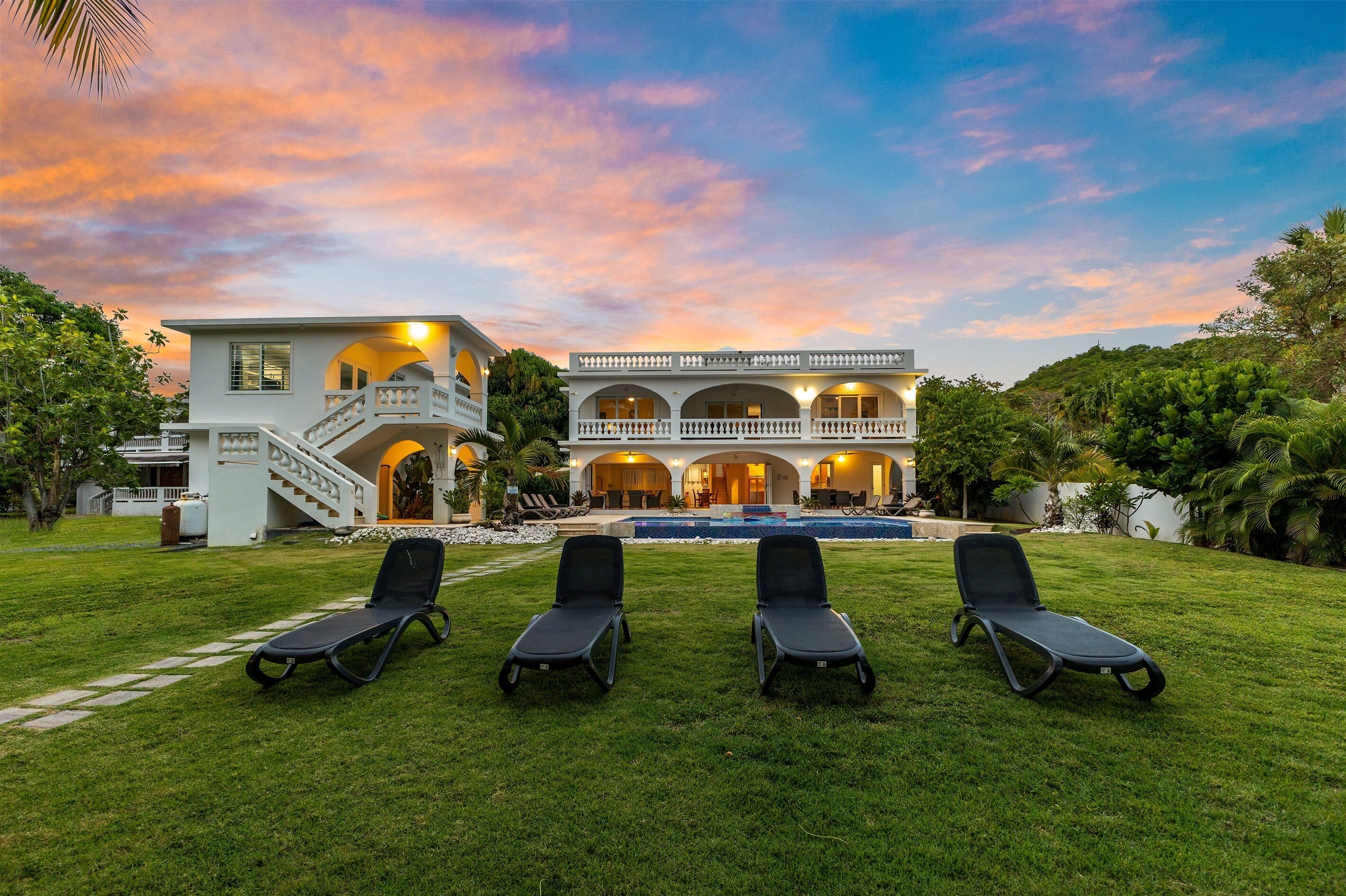 A two-story house with a swimming pool, surrounded by a lawn with four lounge chairs.
