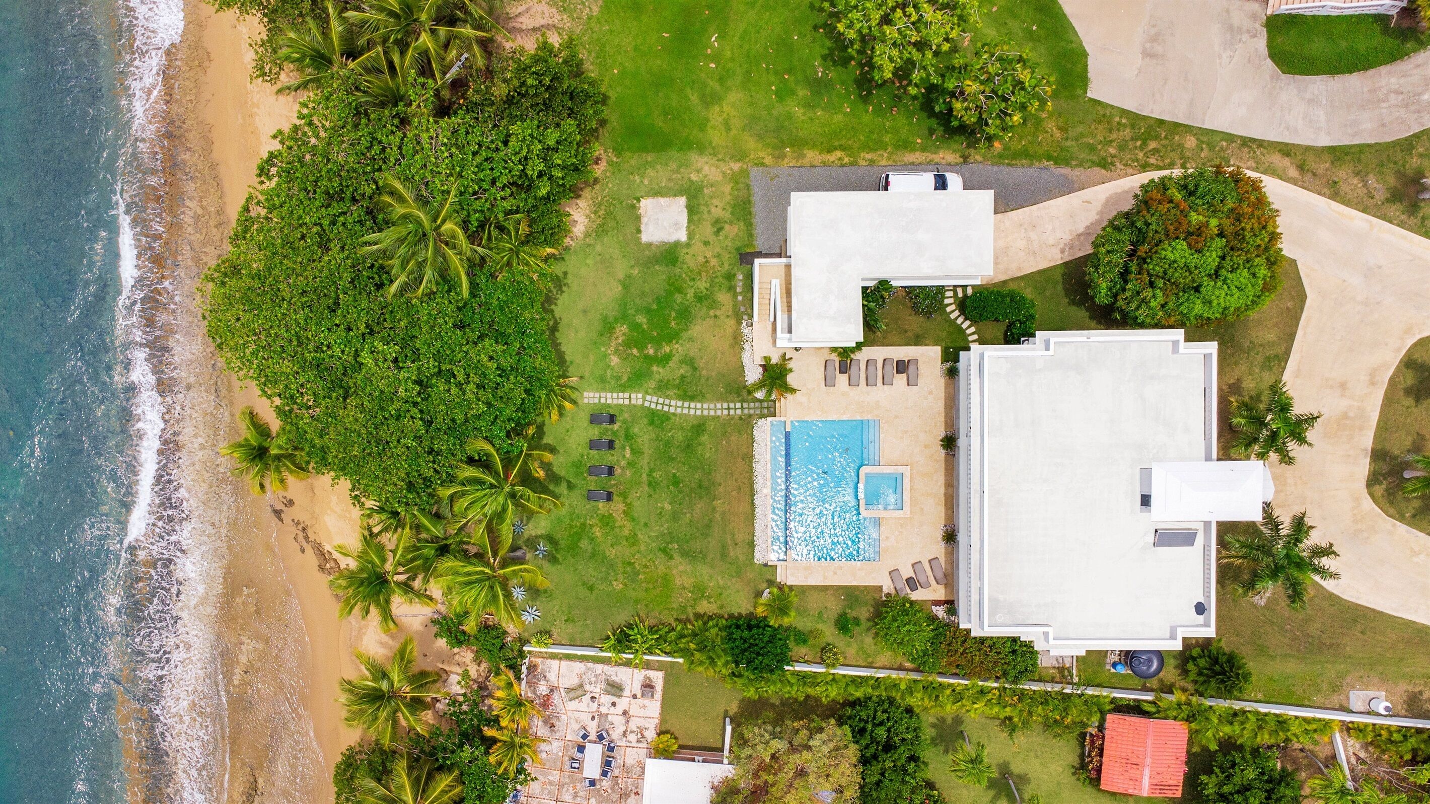 An aerial view of a beachfront property with a swimming pool, multiple lounge chairs, and a large building.