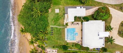 An aerial view of a beachfront property with a swimming pool, multiple lounge chairs, and a large building.