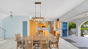 Een ruime eethoek met een houten tafel en stoelen, een keuken op de achtergrond en uitzicht op het omliggende landschap.