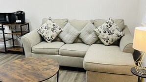 A living room with a sofa, a round coffee table, a lamp, and a microwave on a small table.