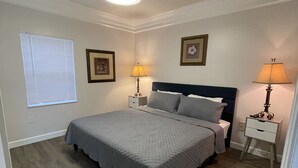 A bedroom with a bed, two bedside tables with lamps, a window with blinds, and a ceiling light.