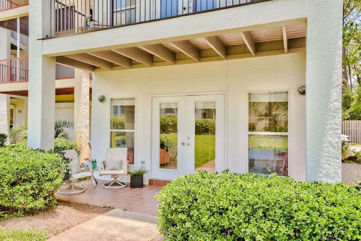 A covered outdoor patio with a seating area, a door with glass panels, and a balcony with railings.