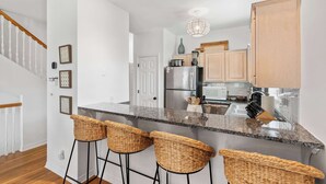 A modern kitchen with a granite countertop, stainless steel appliances, and a bar area with wicker stools. - Fall in Love with Florida!-Now at Reduced Rates (Santa Rosa Beach)