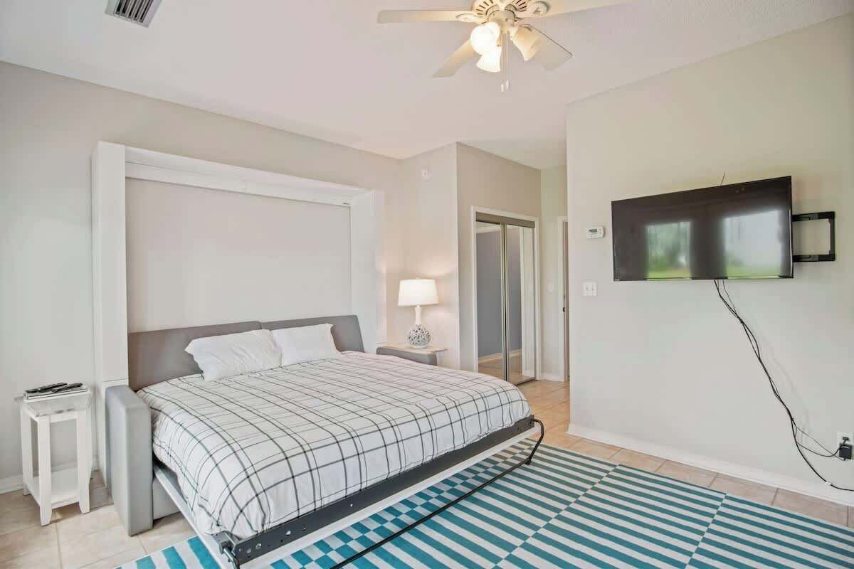 A bedroom with a bed, a nightstand, a lamp, a TV, and a ceiling fan.