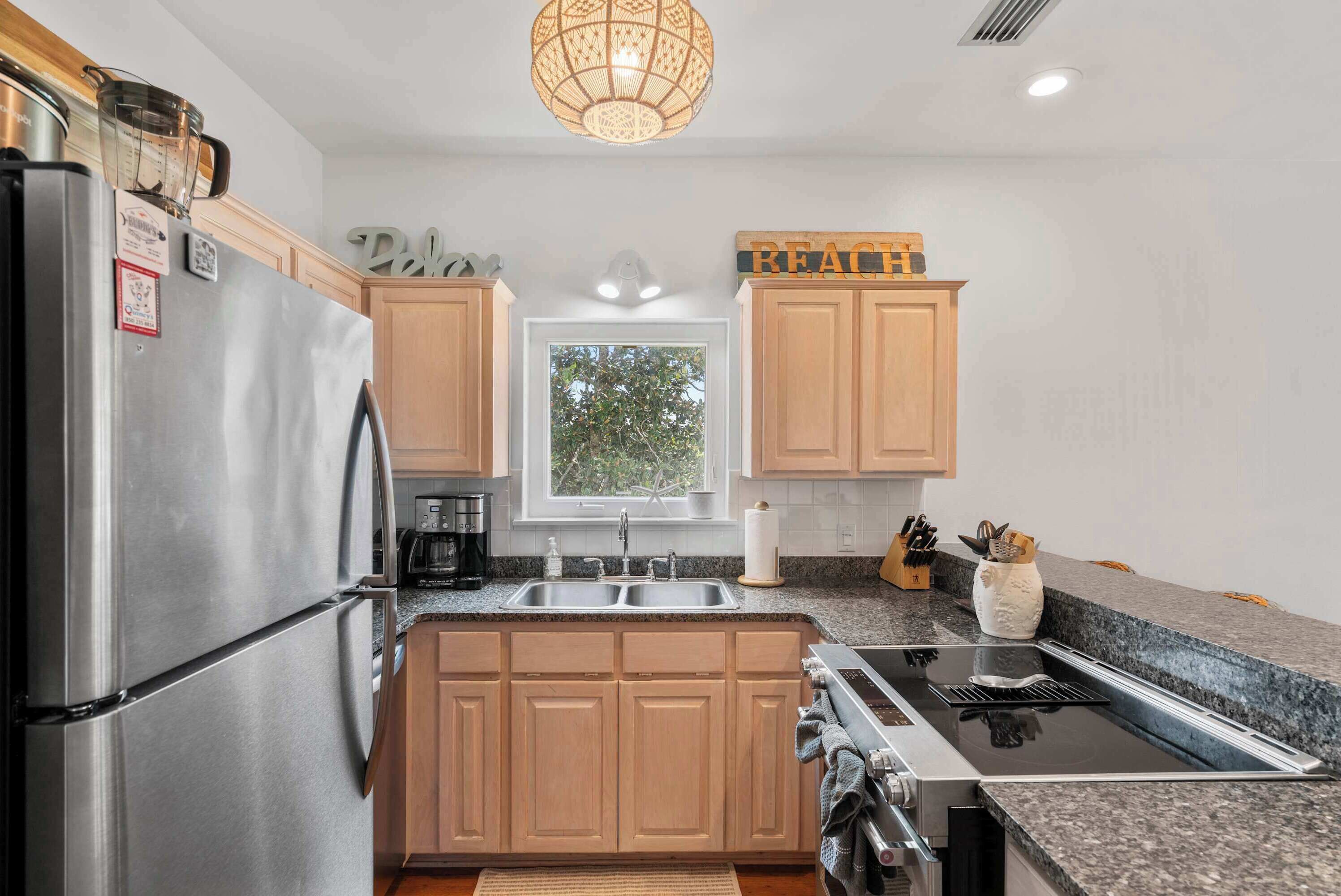 A modern kitchen with wooden cabinets, a stainless steel refrigerator, a built-in stove, and a window with a view of trees.