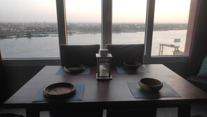 A table with two bowls and a candle in the center, set against a view of a river and cityscape through large windows. -  Nile & Pyramid View – Magical Sunrises, Historic Wonders (Cairo)