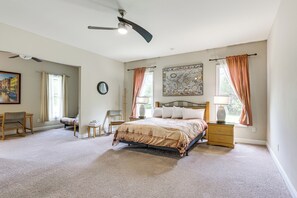 A bedroom with a bed, a desk, a chair, a window with curtains, a ceiling fan, and a wall clock.