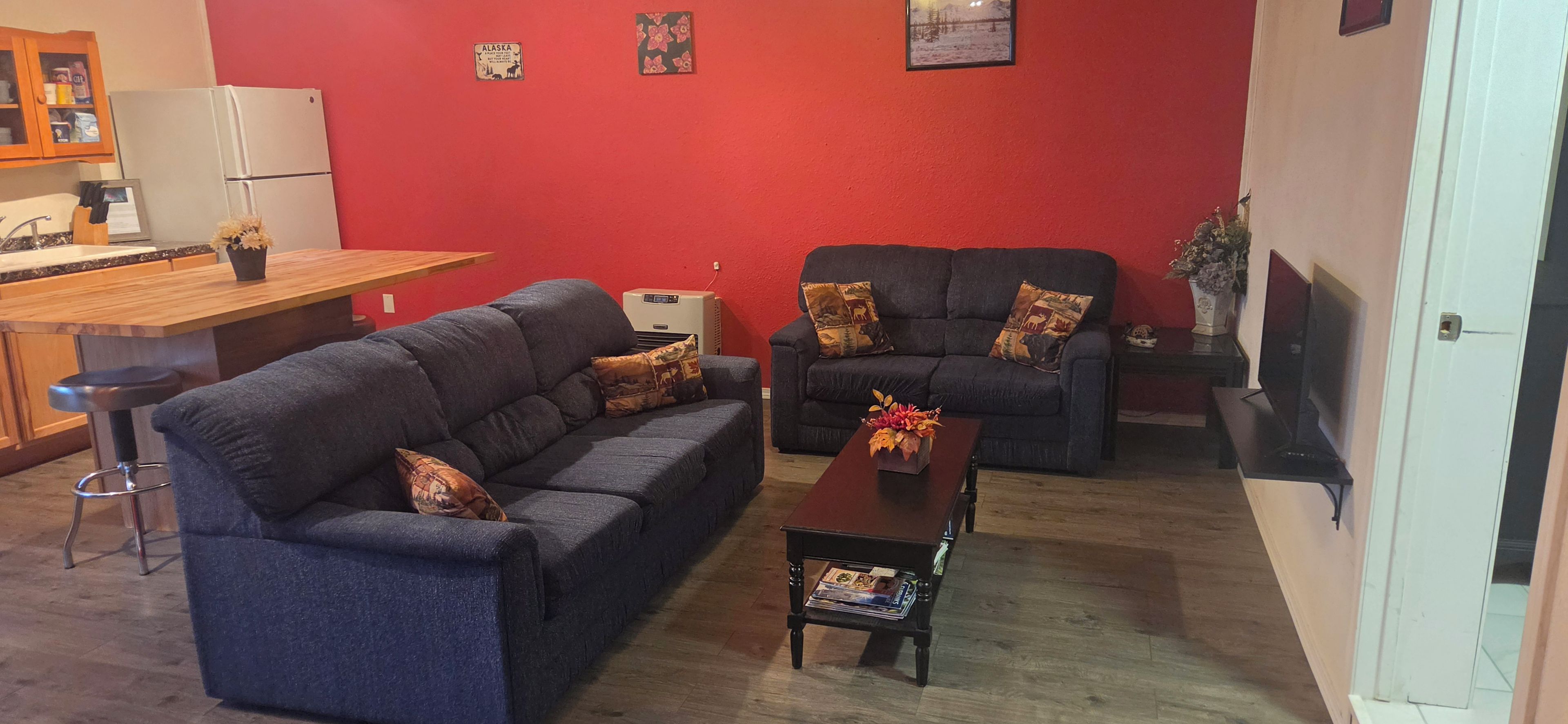 A living room with two sofas, a coffee table, a kitchen area with a refrigerator, and a dining table.