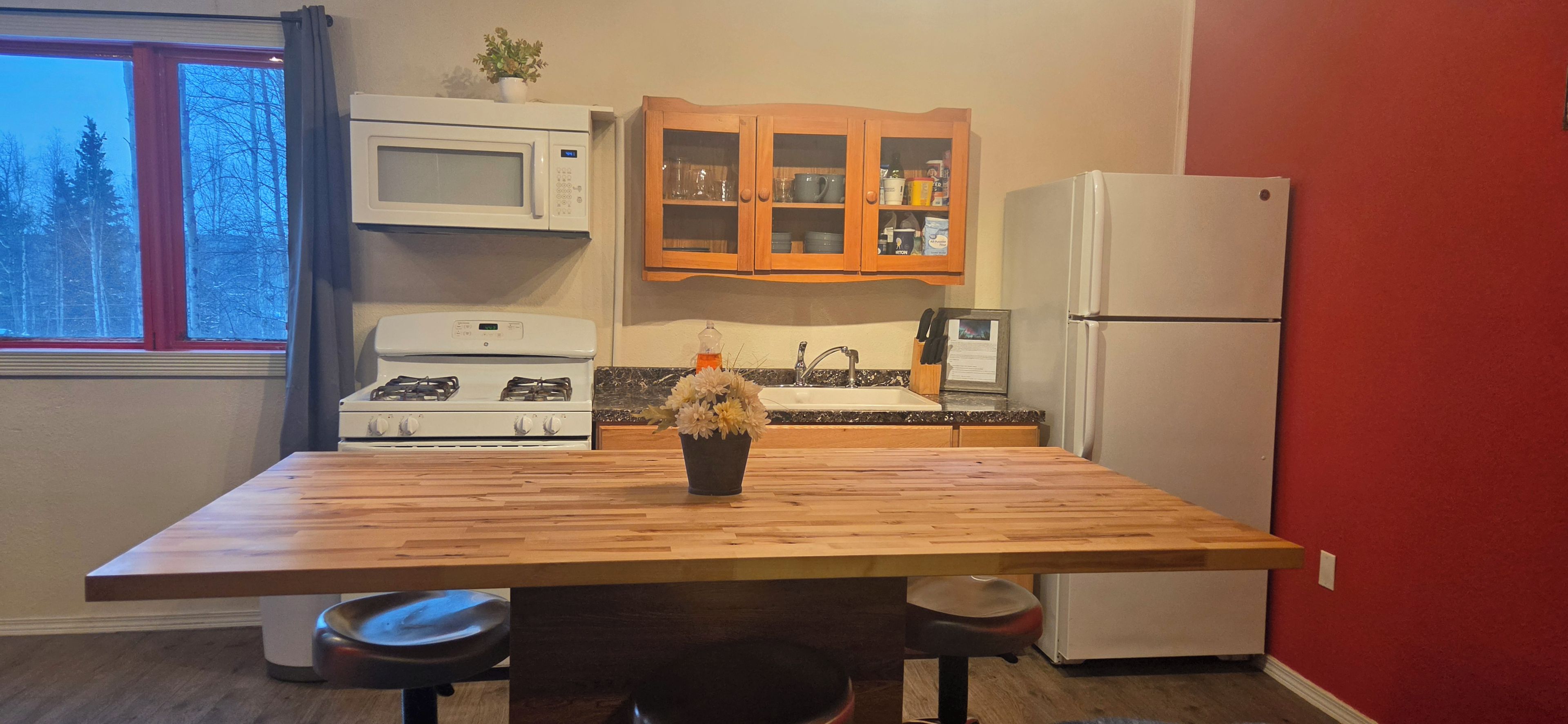 A kitchen with a wooden table, a stove, a microwave, a refrigerator, and a cabinet with glass doors.