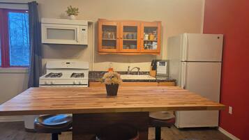 A kitchen with a wooden table, a stove, a microwave, a refrigerator, and a cabinet with glass doors.