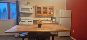 A kitchen with a wooden table, a stove, a microwave, a refrigerator, and a cabinet with glass doors.