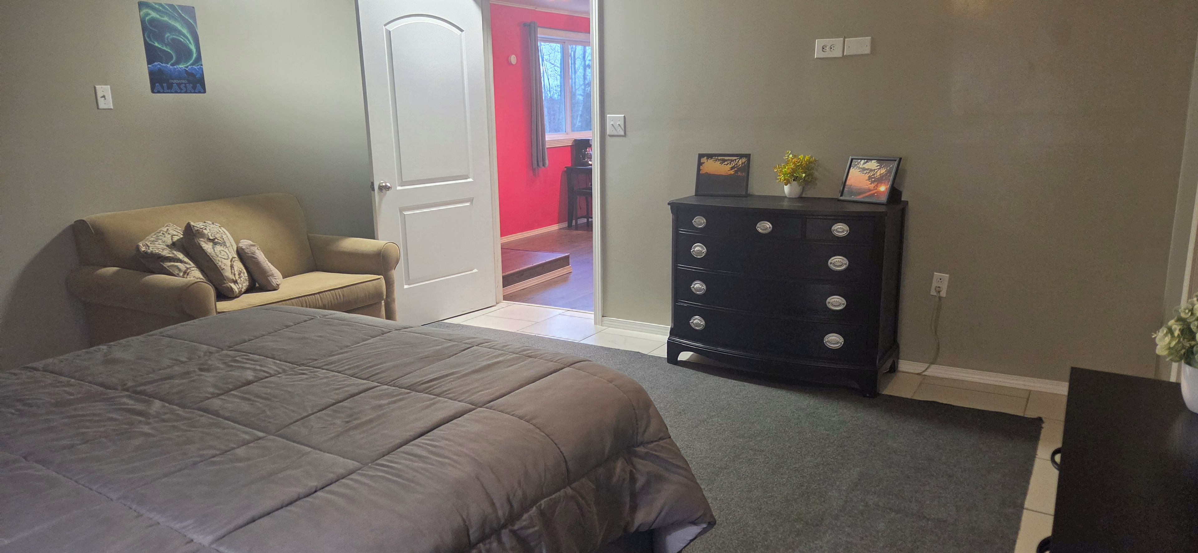 A bedroom with a bed, a dresser, a chair, and a door leading to another room.