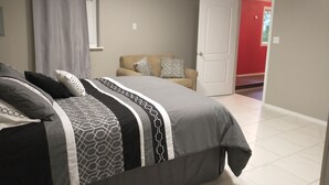 A bedroom with a bed, a sofa, a door, and a window.