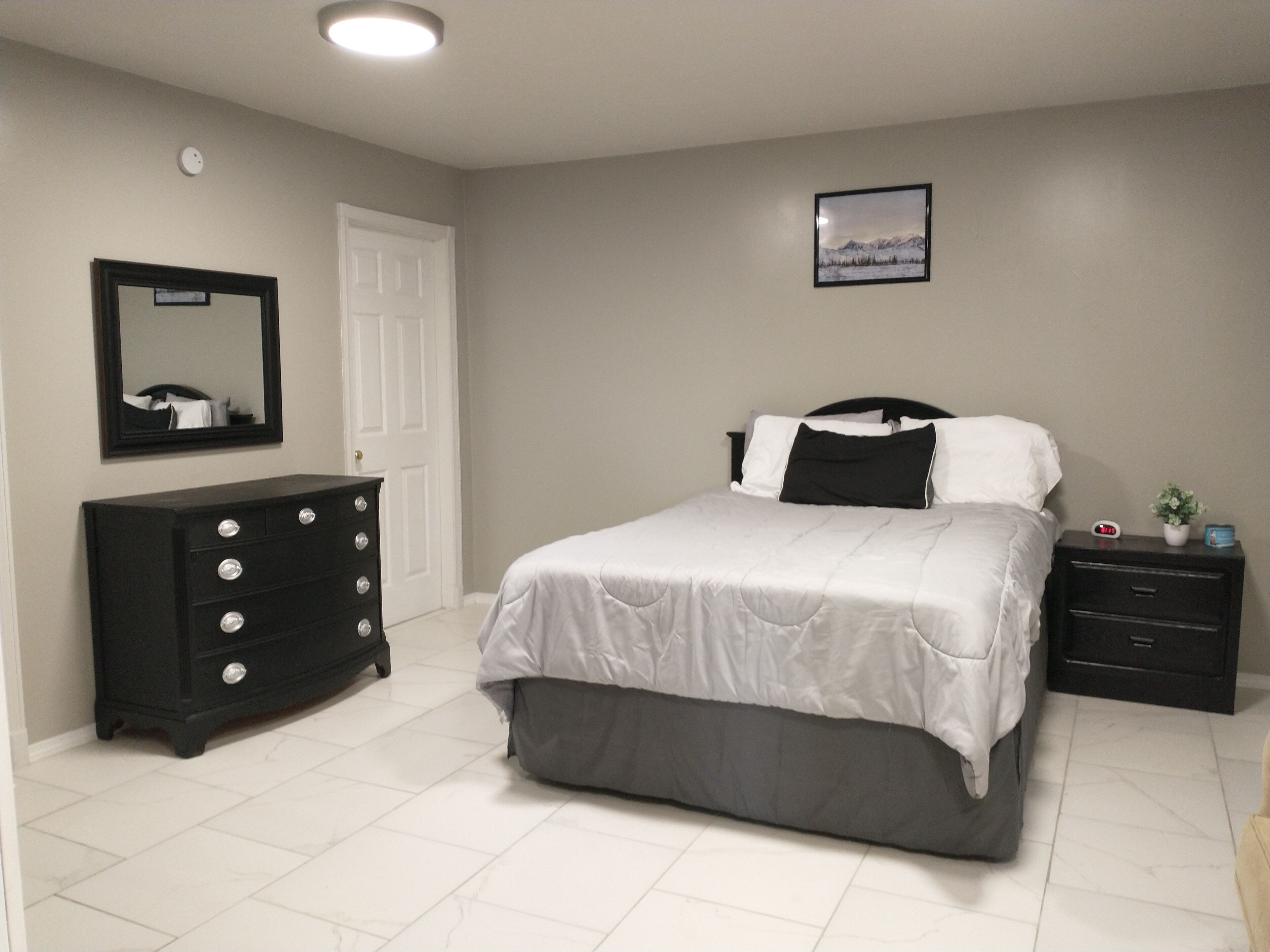 A bedroom with a bed, dresser, nightstand, and a wall-mounted picture.