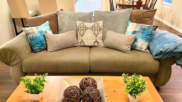 A sectional sofa with multiple cushions and two potted plants on a wooden table.