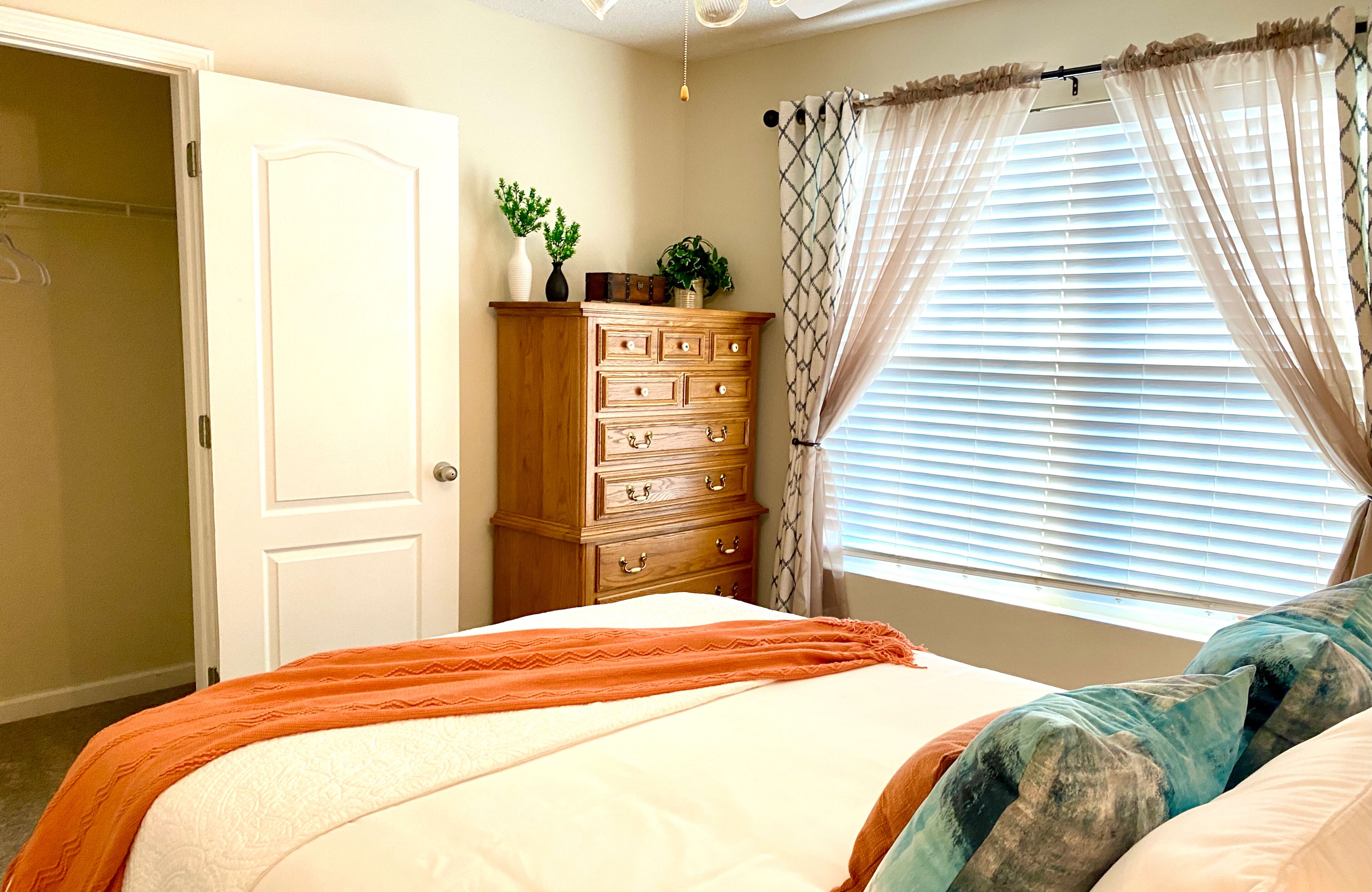 Une chambre à coucher avec un lit, une commode, une fenêtre avec des stores et une porte.