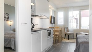 A compact kitchen with modern appliances, a dining area with a table and chairs, and a bed in the adjacent room.