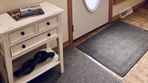 Une pièce avec une commode blanche, un miroir, une porte ornée d’un miroir ovale et une fenêtre avec des stores.