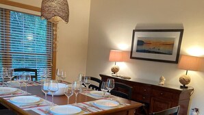 Un coin repas avec une table en bois dressée pour six personnes, des chaises, un luminaire suspendu et une lampe fixée au mur.