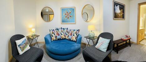 Een woonkamer met een blauwe bank, twee fauteuils, een salontafel en een schilderij aan de muur.