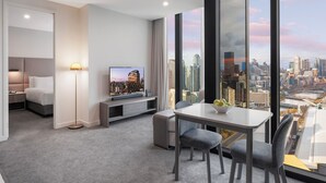 Ein modernes Hotelzimmer mit Blick auf die Stadt, einem Flachbildfernseher, einem Essbereich und einem Bett.