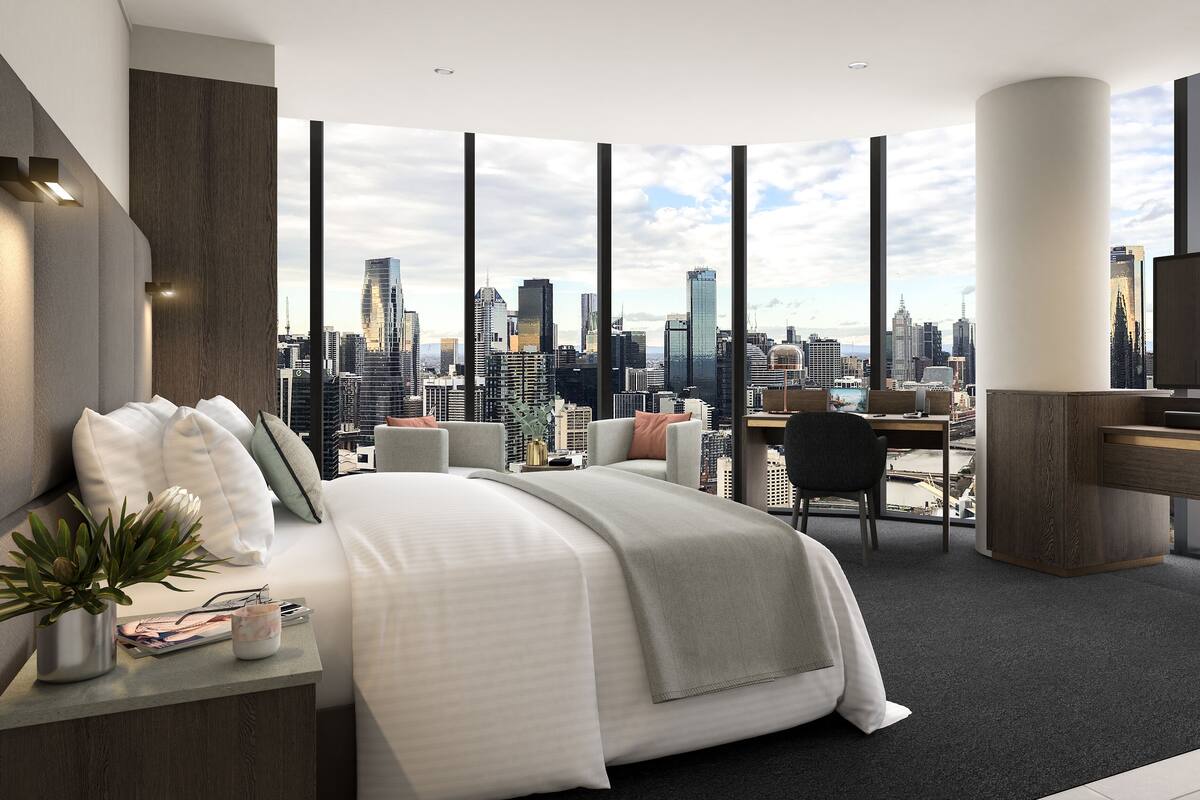 A modern hotel room with a large bed, a desk, and a TV. The room has a city view through large windows.