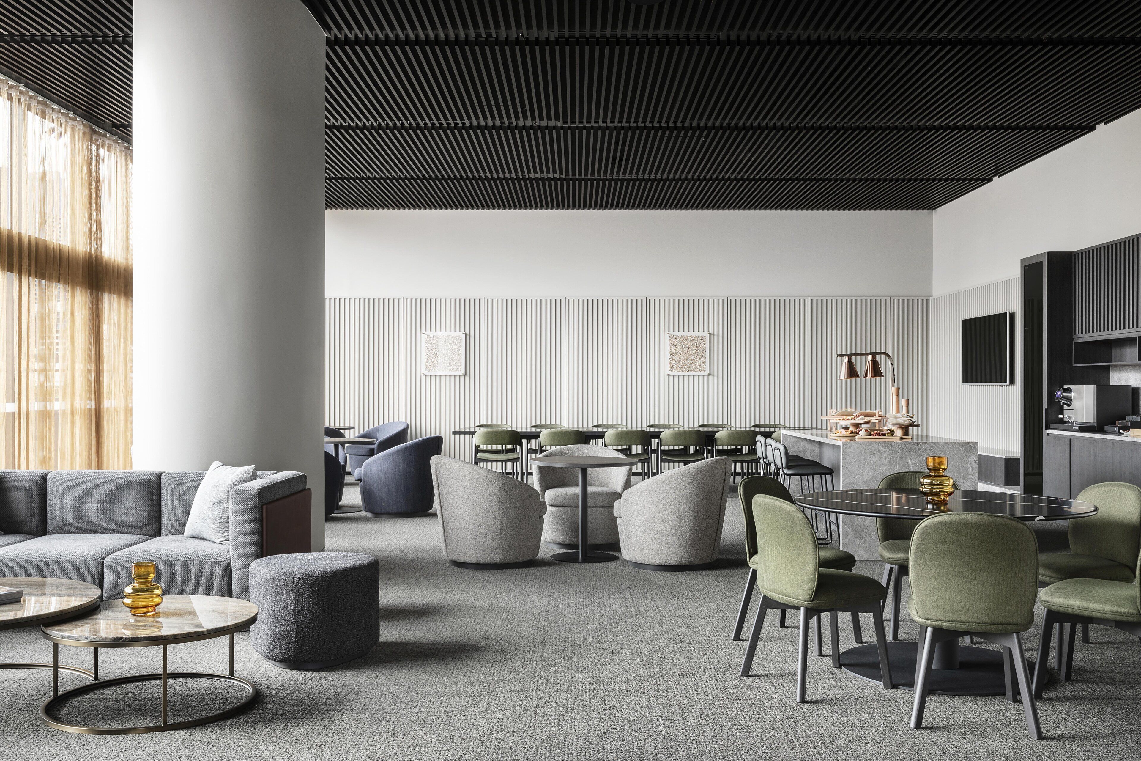 A modern interior with a grey sofa, round tables, green chairs, and a kitchen area.