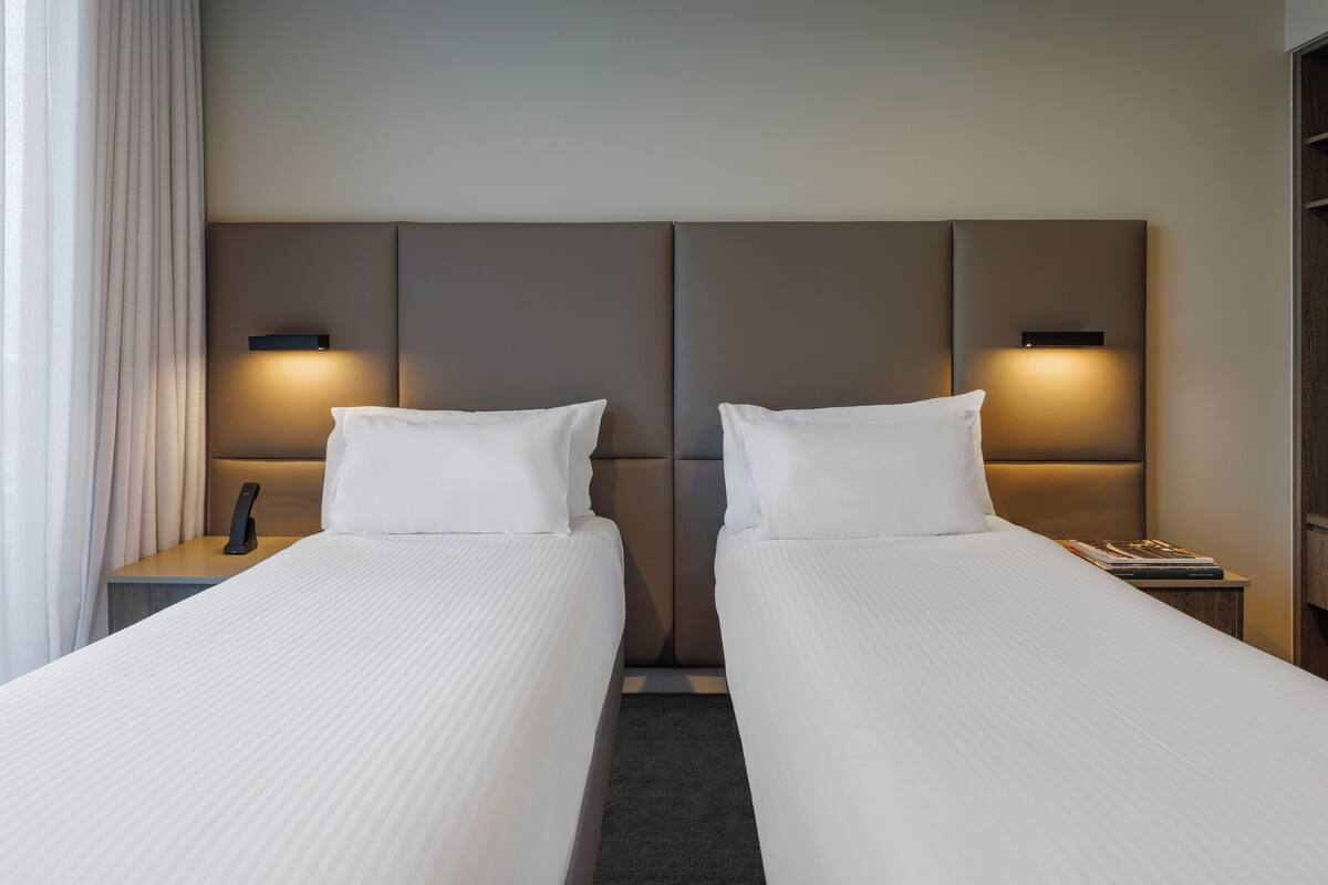 A hotel room with two beds, each with a headboard, bedside tables, and lamps.