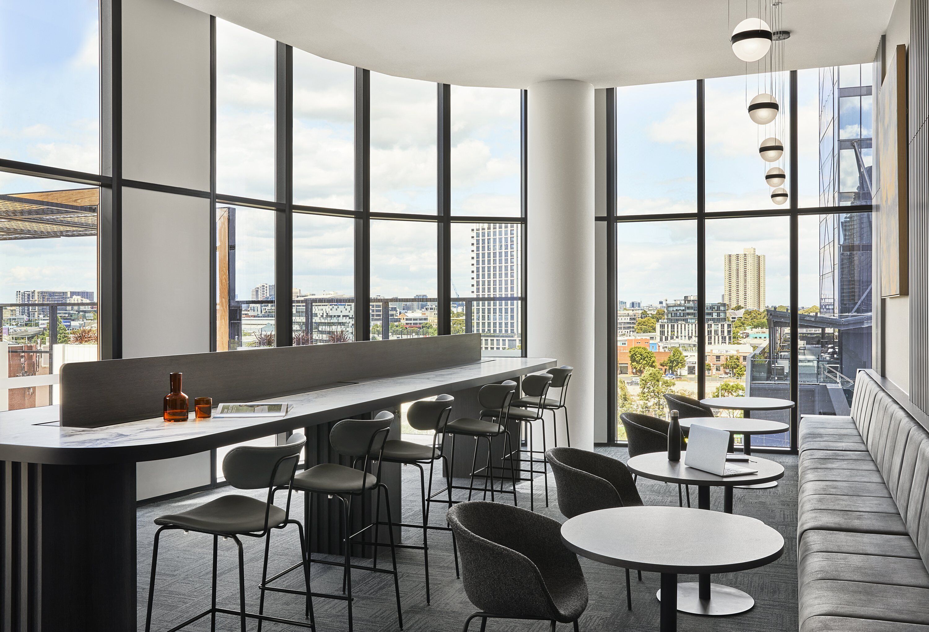 Zona de bar moderna con techos altos y grandes ventanales que ofrecen vistas a la ciudad.