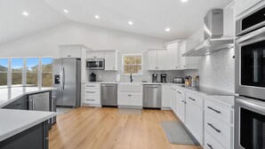 A modern kitchen with white cabinetry, stainless steel appliances, and a wooden floor. - Lakeview Home/Private Boat Dock/Hot tub/Golf Cart/Gameroom/Stunning Fall Views (LaFollette)