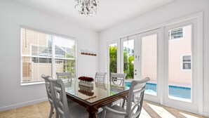 A dining area with a glass table, white chairs, and a view of a swimming pool. - Private Pool | Reunion Membership | 8 Miles to Disney (Kissimmee)