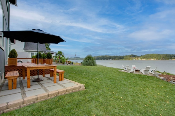 Un patio con mesa y sillas, un parasol grande y vista a un lago.