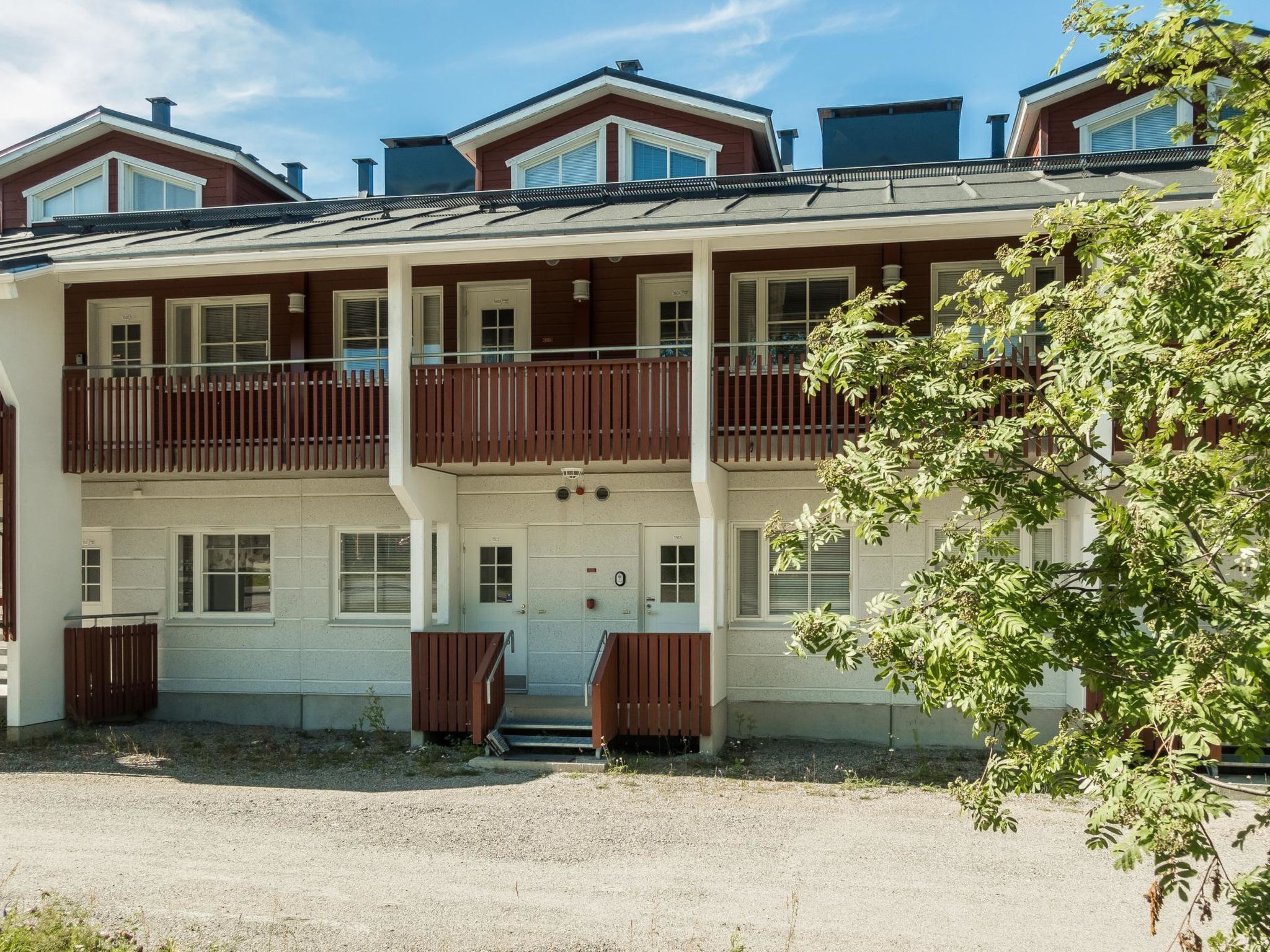 A multi-story building with a central entrance, balconies, and a gravel driveway.