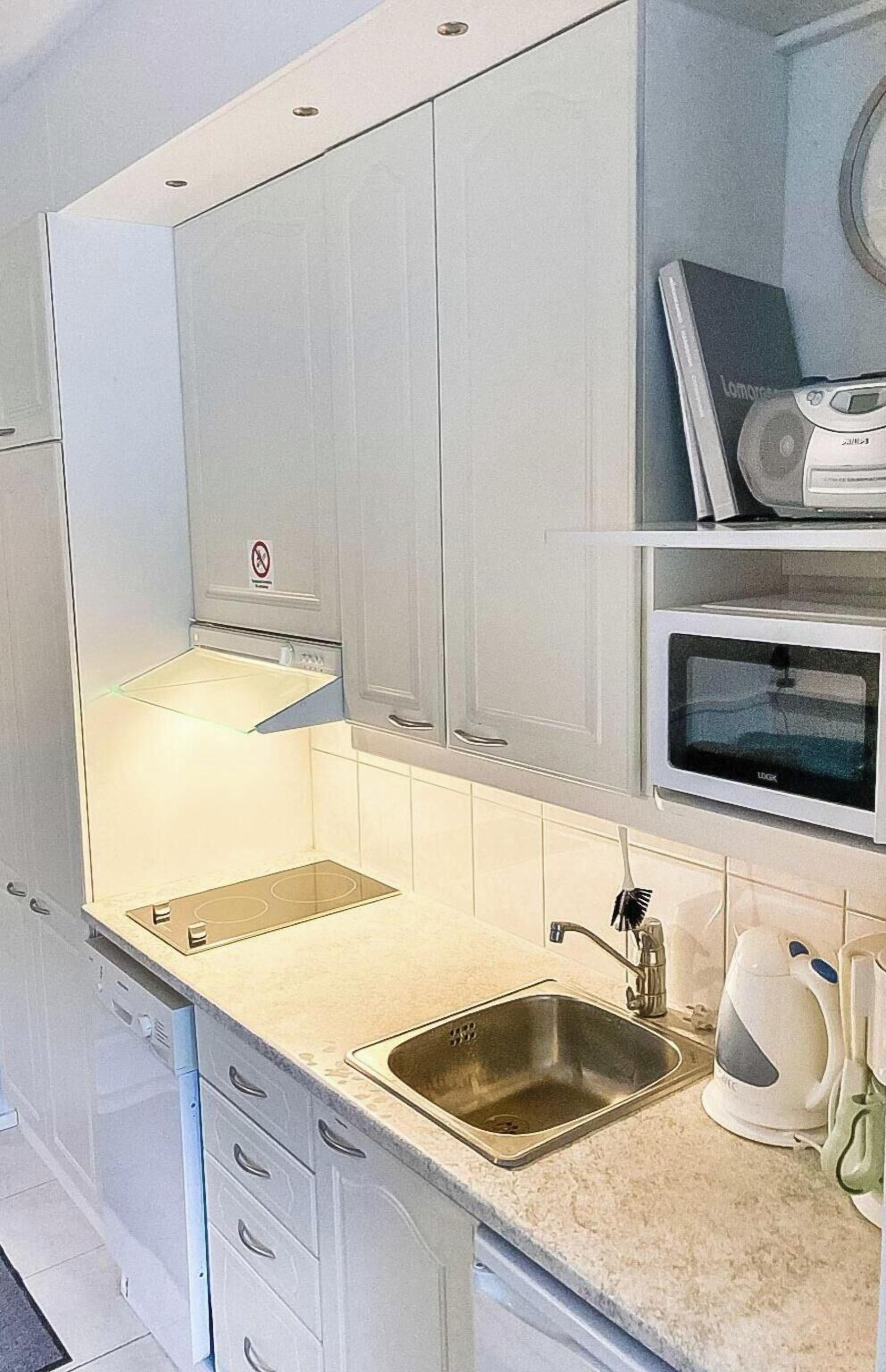 A modern kitchen with white cabinets, a stainless steel sink, a microwave, and a kettle.