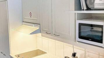 A modern kitchen with white cabinets, a stainless steel sink, a microwave, and a kettle.