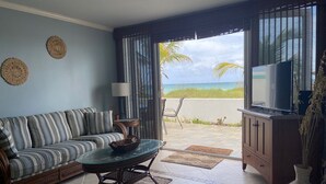 A living room with a sofa, a glass-top coffee table, a TV, and a view of the ocean.