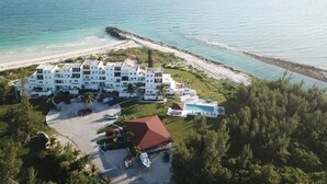 A beachfront hotel with multiple buildings, a parking area, and a view of the ocean.