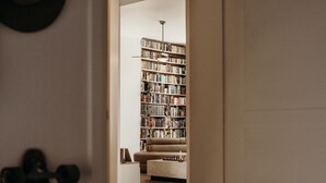 En døråbning ind til en stue med et stort bogreol, en sofa og en loftsvift.