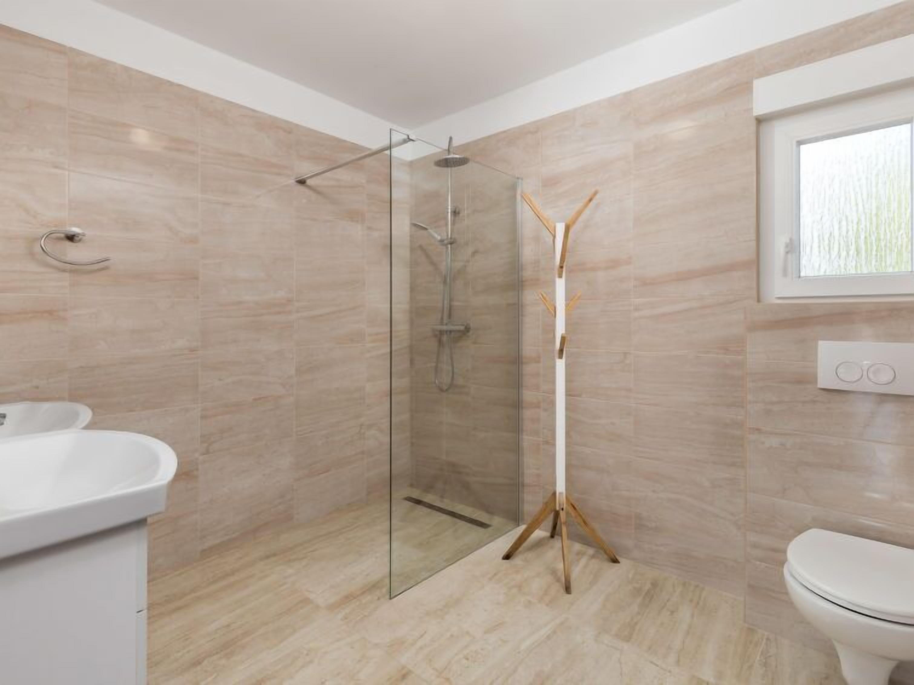 A modern bathroom with a glass-enclosed shower, a white sink, and a toilet.