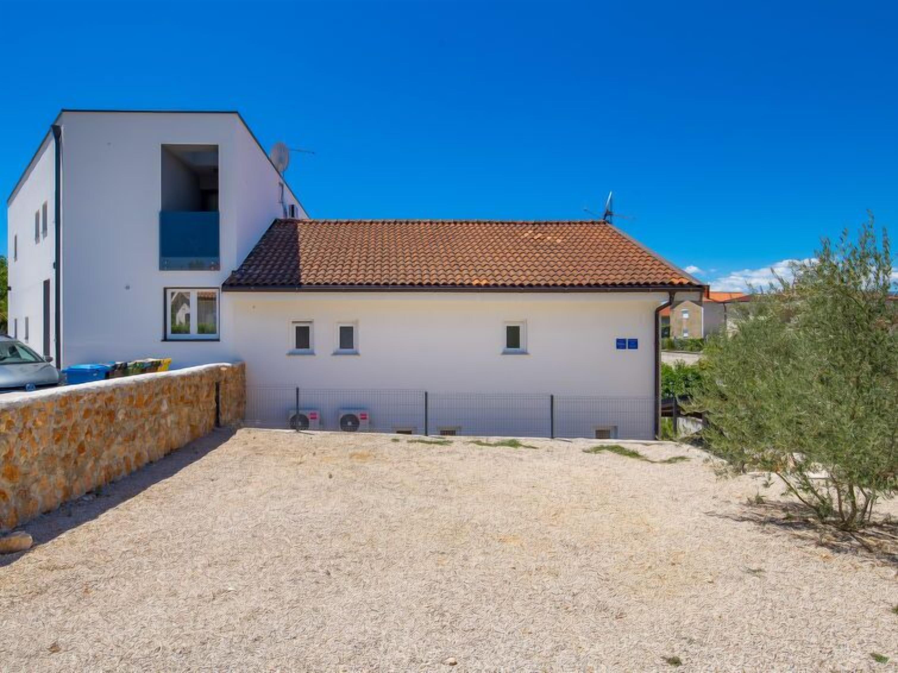 Un edificio de dos pisos con techo de tejas, pared de piedra y entrada de grava.