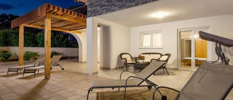 A covered outdoor area with lounge chairs, a wooden pergola, and a stone wall.