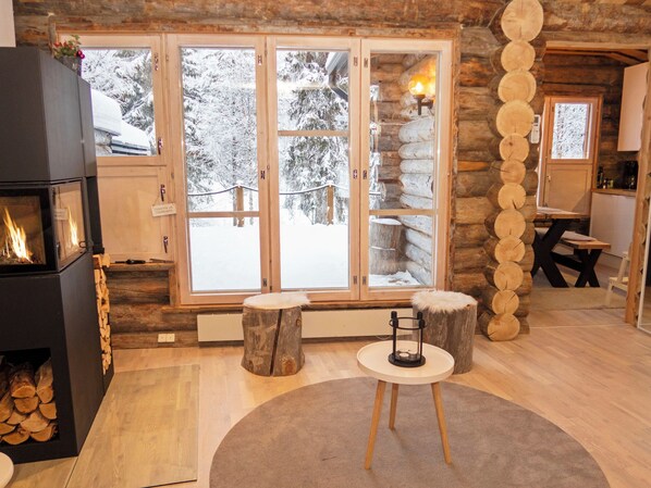 A log cabin interior with a fireplace, a dining area, and a view of a snowy landscape through large glass doors.